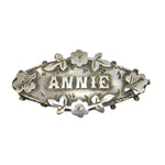 Silver brooch with 'ANNIE' engraved on a gray background