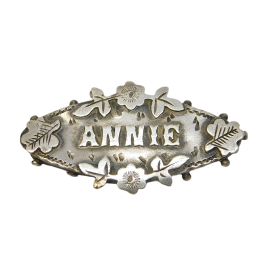 Silver brooch with 'ANNIE' engraved on a gray background