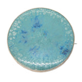 Round turquoise brooch with gold edge on a white background