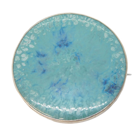 Round turquoise brooch with gold edge on a white background