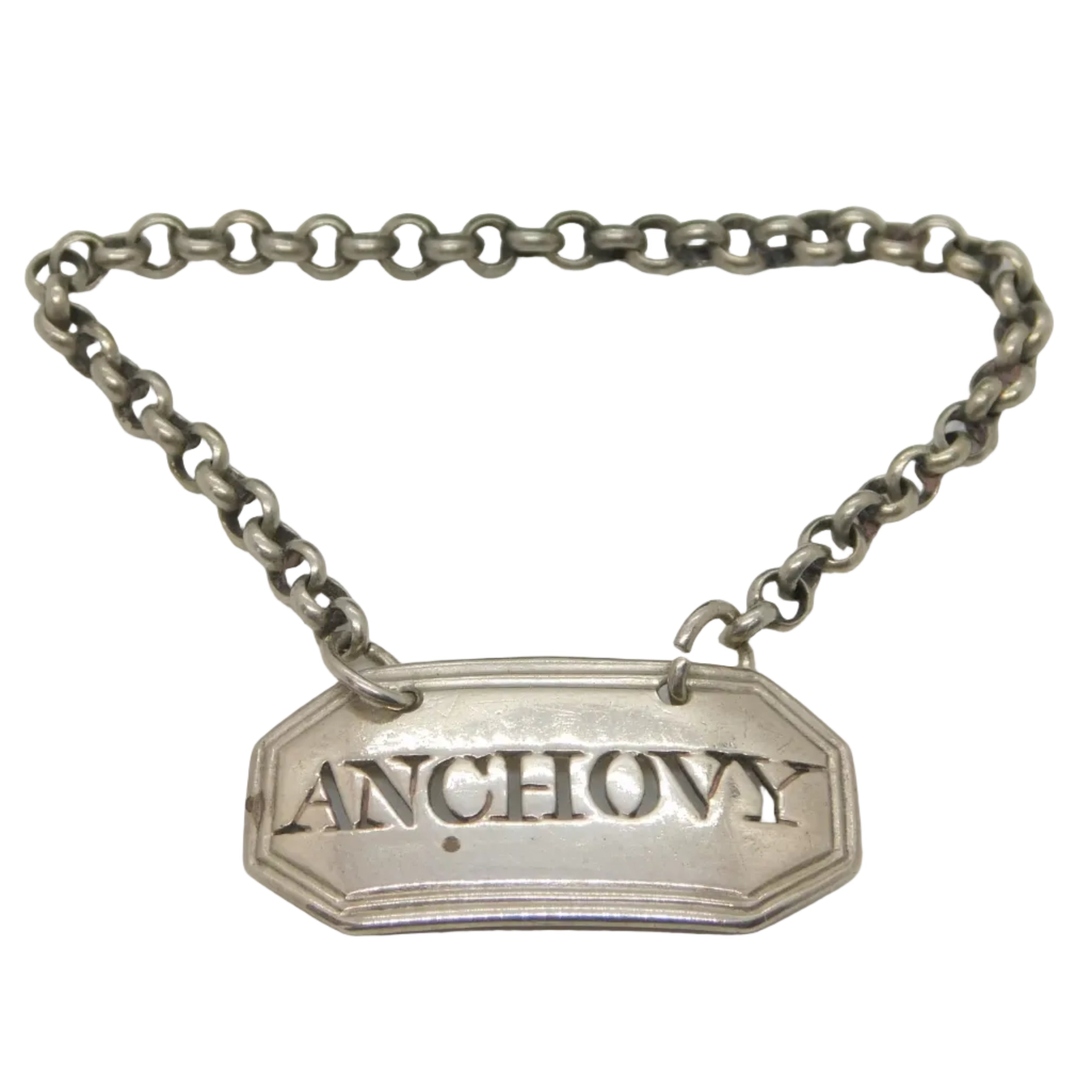 An antique Georgian sterling silver 'Anchovy' sauce bottle label with intricate detailing and the word 'ANCHovy' printed on it, accompanied by a small chain. The label is marked with faint makers' marks.