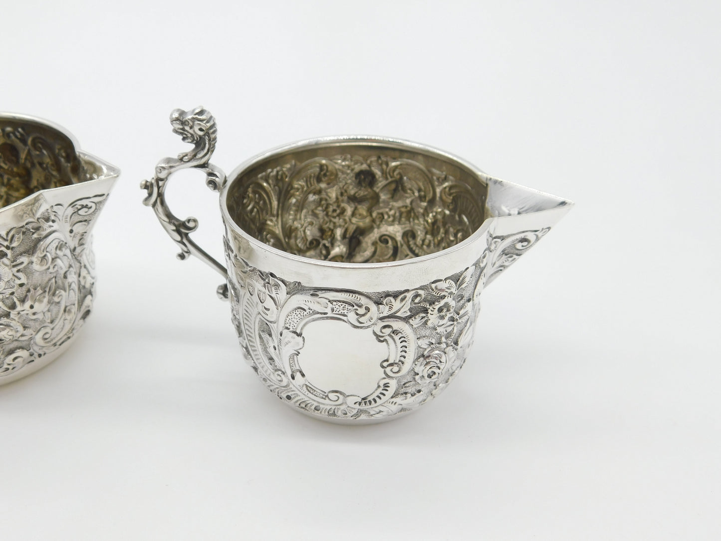 Pair Victorian Sterling Silver Cupid, Floral, Mythic Cream Jugs Antique 1900