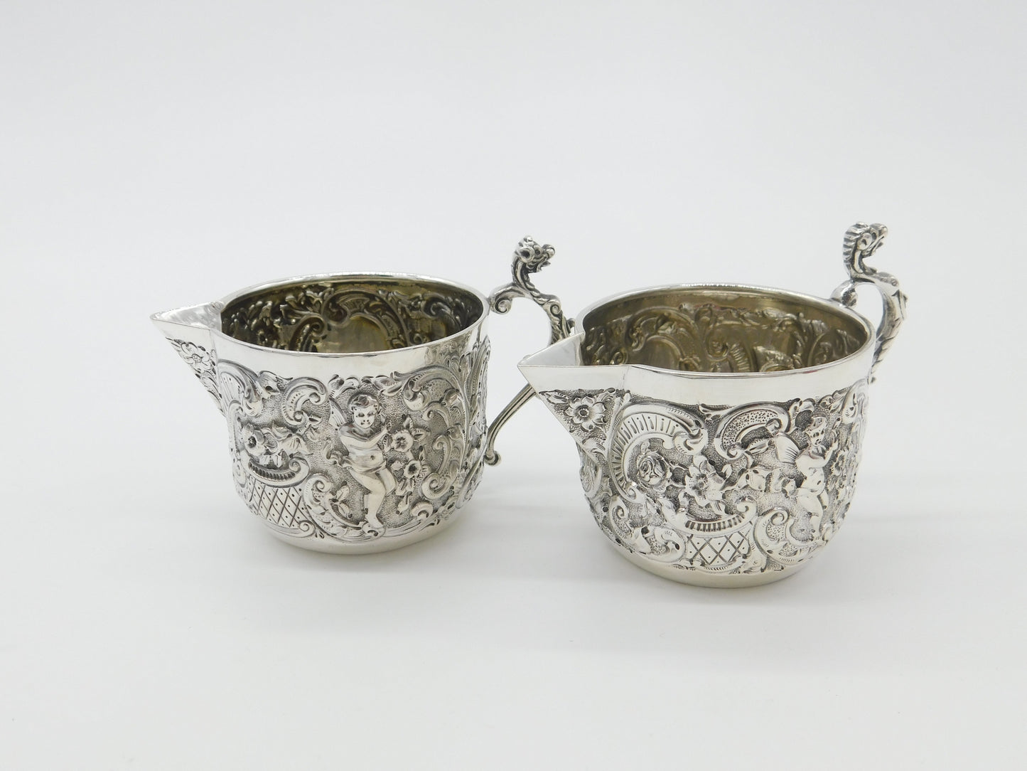 Pair Victorian Sterling Silver Cupid, Floral, Mythic Cream Jugs Antique 1900