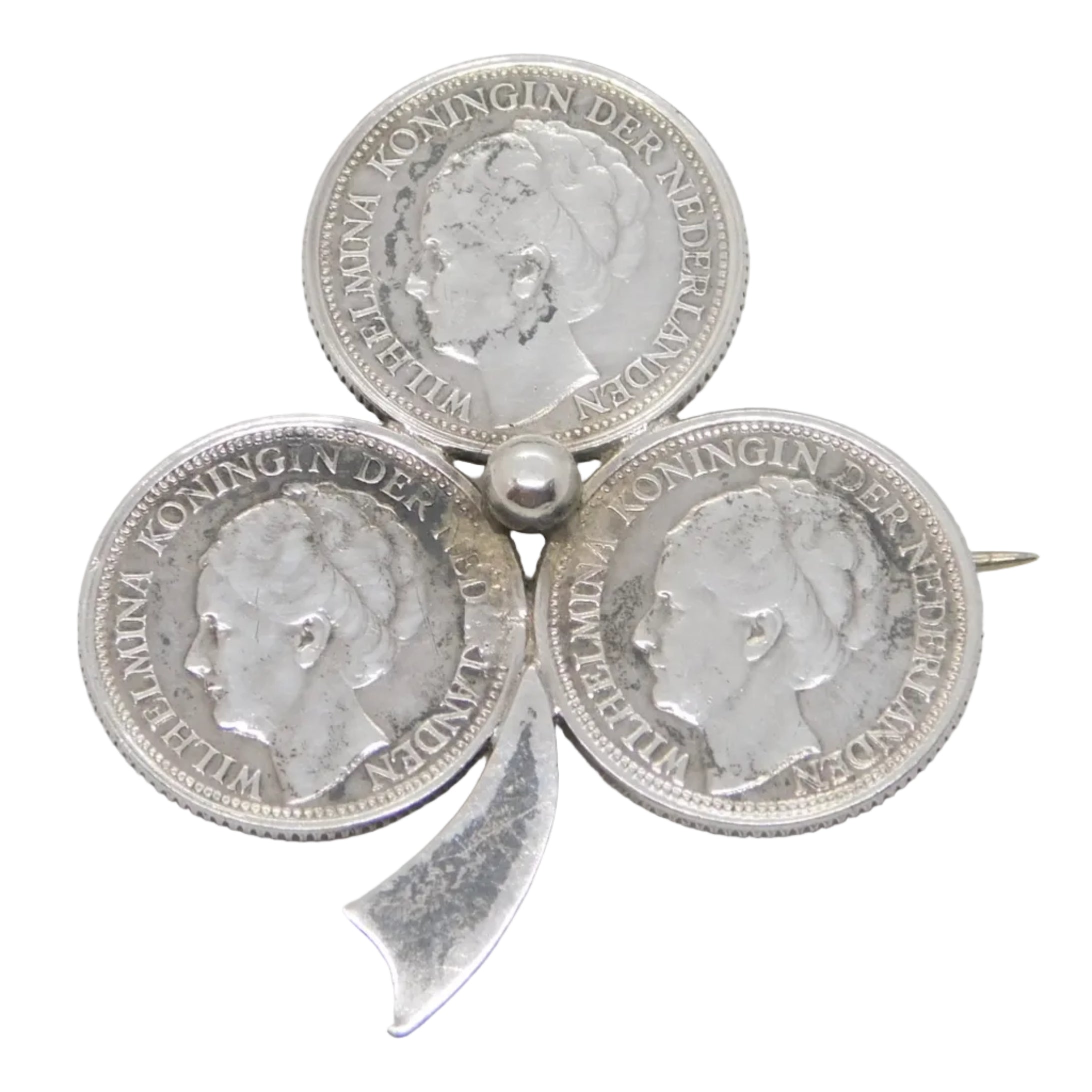 An antique silver brooch featuring a shamrock design with four coins, presented on a white surface with a brown box in the background.