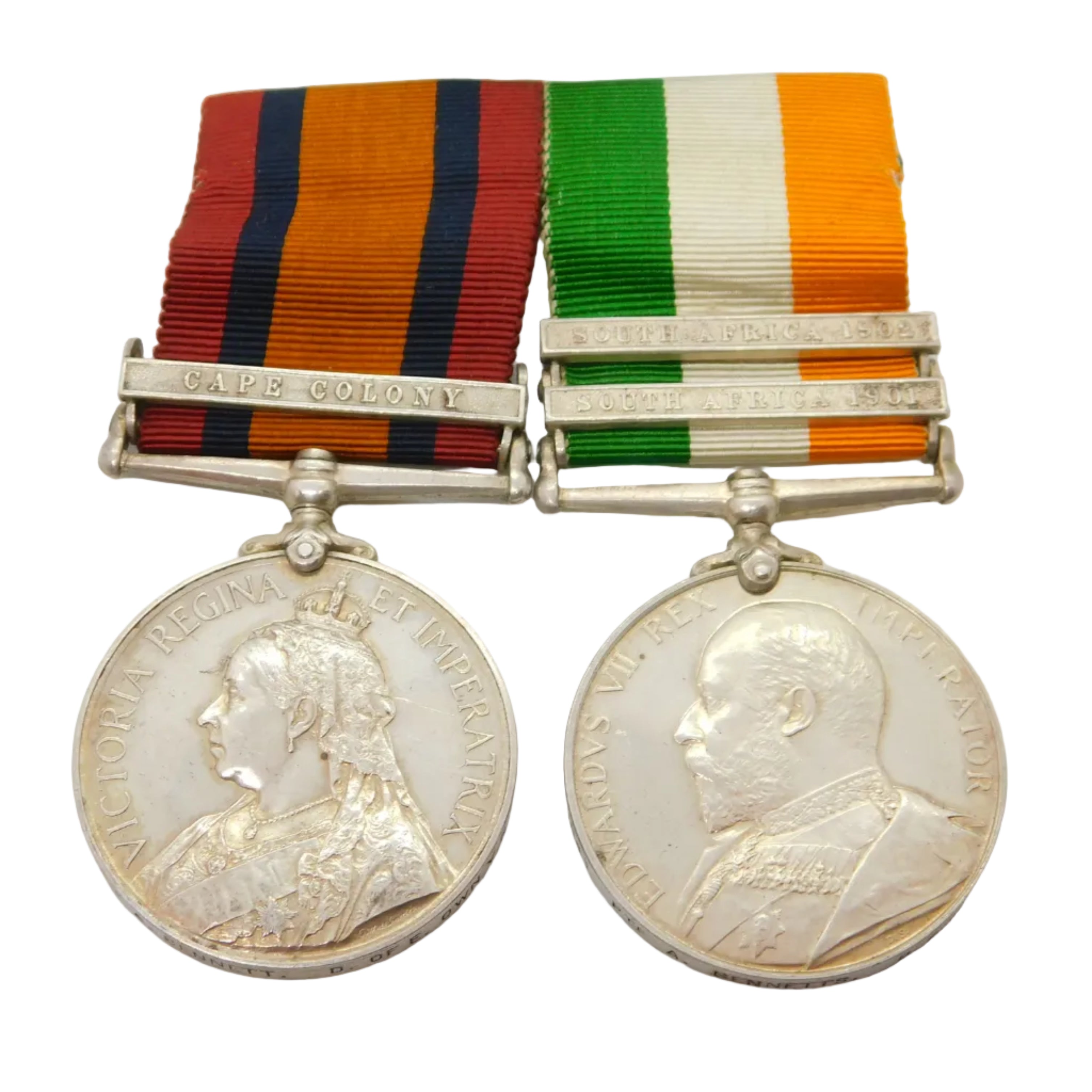 A silver medal with a portrait of Queen Victoria, accompanied by a red and blue ribbon, and a second silver medal with a different portrait, all laid on a white surface.