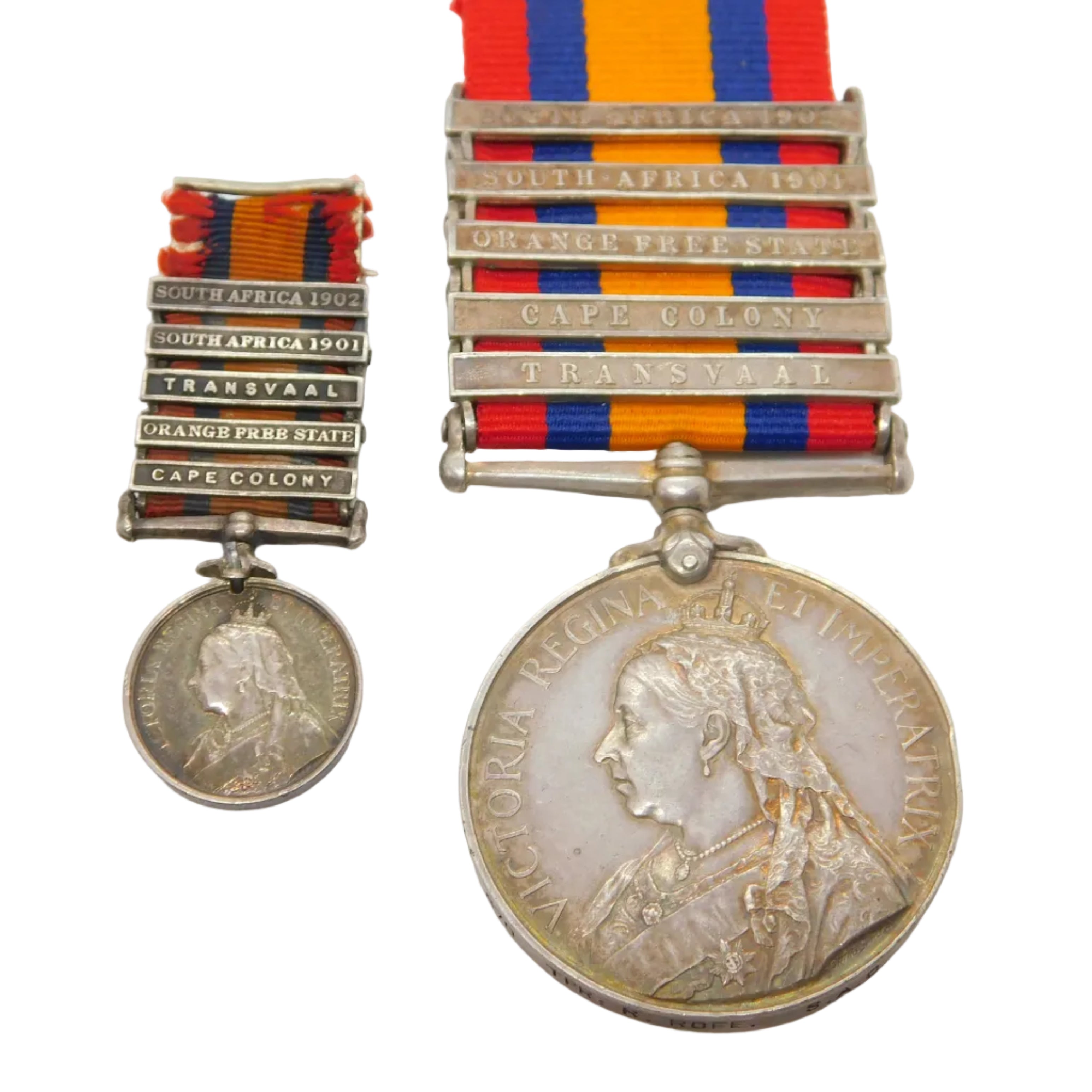 A silver-colored antique medal with a red and blue ribbon and a second, smaller medal attached by a ribbon, both featuring inscriptions and a portrait.